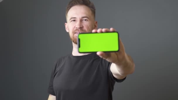 髭を生やした男が緑色の画面をした携帯電話を見せて笑顔で喜ぶ — ストック動画