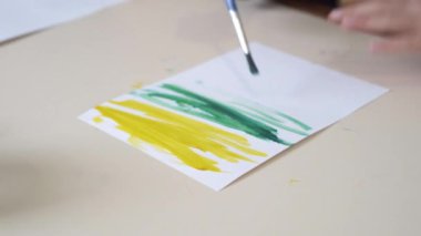 Çocuk bir kağıt parçasına gouache çizer.