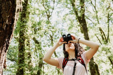 Büyük bir ormanda dürbünden bakan bir kadın.