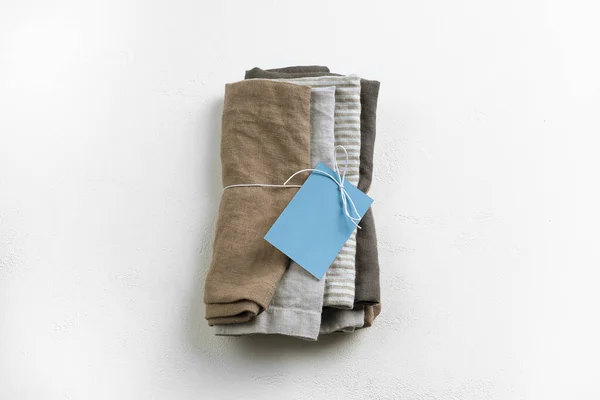 4つの茶色 縞模様と濃い灰色の純粋なリネンや生の綿のナプキンパックのキッチン繊維のセットは テキストのためのコピースペースとテクスチャ化された白いコンクリートの背景に白いリボンと空の青いカードでパック Rの設定を提供するためのタオルやタオル — ストック写真