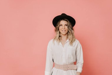 Beyaz bluzu ve açık pembe duruşu olan şapkalı, sevimli, güler yüzlü sarışın, kendine güvenen, pembe arka planda fotokopi çeken. Tarz ve alışveriş konsepti.
