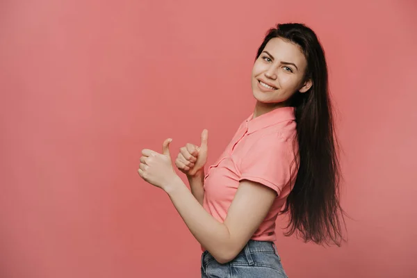 Pembe arka plan başarısı tabelasının üzerine pembe tişört giyen genç, güzel esmer kadın. Elleriyle olumlu jest yapıyor. Gülümsüyor ve mutlu. Neşeli ifade ve kazanan