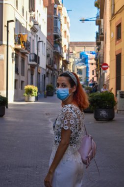 Coronavirus karantinası sırasında cerrahi maske takan bir kadın parkta yürüyor.