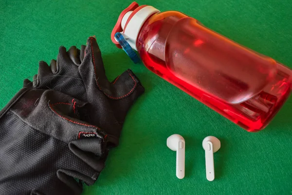 Sports tools for training put on a green background, gloves, bottle for drinks, wireless headphones, fitness