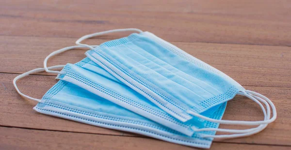 Ağız ve burnu kaplayan, havada yayılan virüslerden korunmak için tahta bir zemine yerleştirilmiş 3 parça mavi tıbbi koruyucu maske. Sağlık hizmetleri ve tıbbi kavramlar