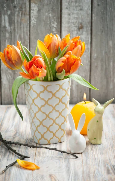 Ramo de tulipanes anaranjados, velas encendidas y conejos de Pascua —  Fotos de Stock