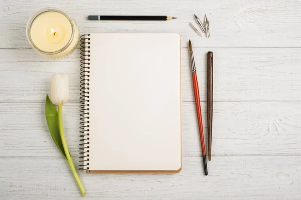 Caderno aberto, lápis, vela, pincéis e tulipa — Fotografia de Stock