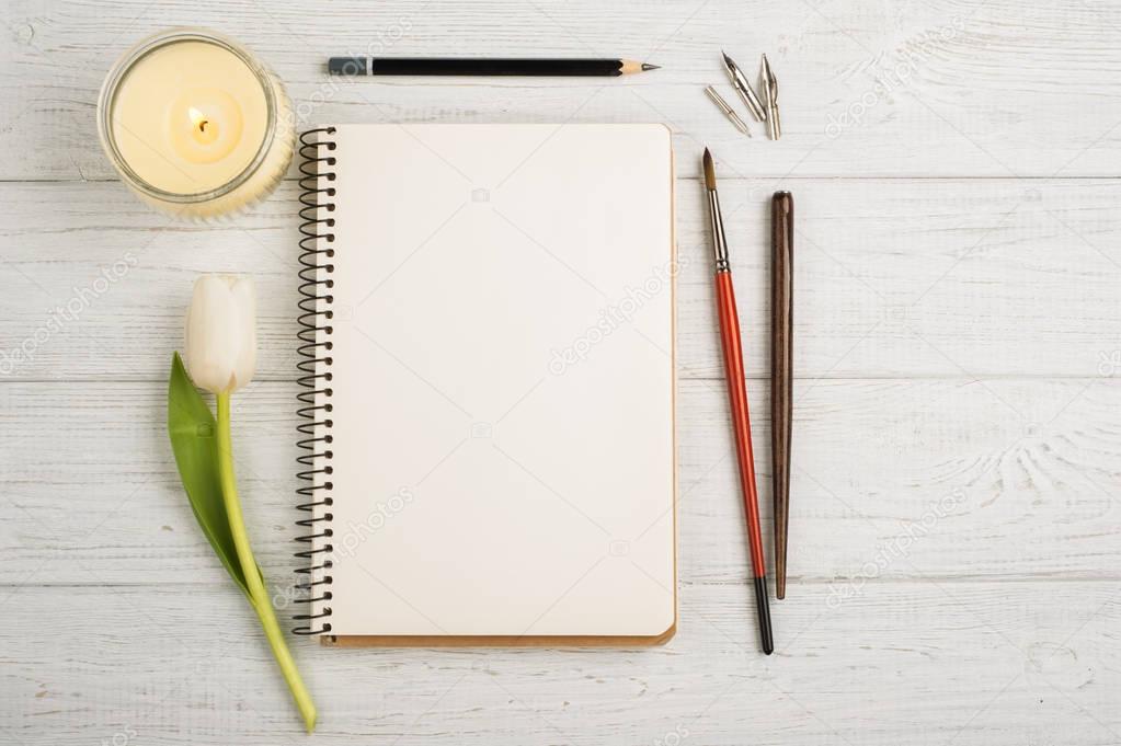 Open notebook, pencil, candle, brushes and tulip