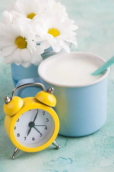 A mug of milk with straw, yellow alarm clock and flowers — Stock Photo, Image