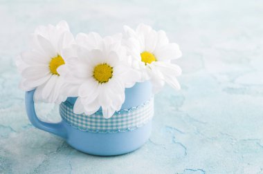 Eski püskü bir beton yüzey üzerinde papatya ile mavi kupa