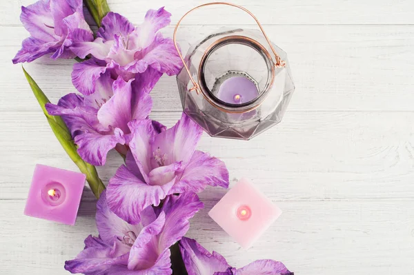Paarse gladiolen en aangestoken kaarsen op witte tafel — Stockfoto