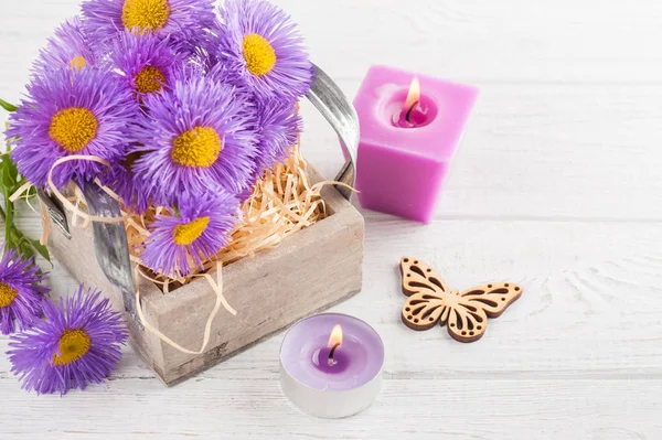 Marguerites violettes et bougies allumées sur table blanche — Photo