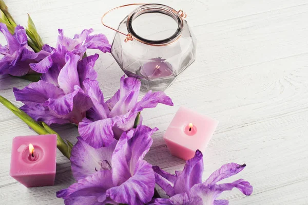 Фиолетовый гладиолус и зажженные свечи на белом столе — стоковое фото