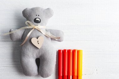 Beyaz masada kırmızı ve turuncu kalemli gri sevimli oyuncak ayı. Tebrik kartı ya da metin için alanı kopyala