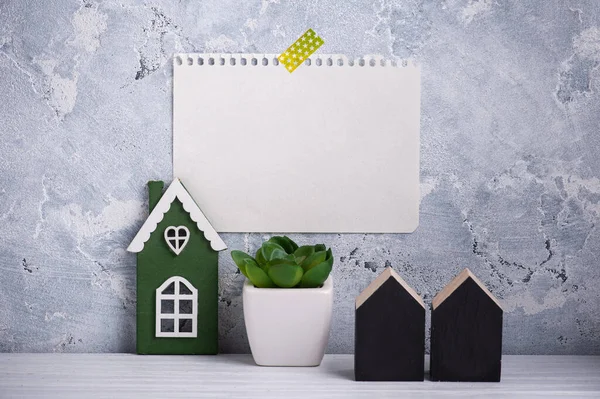 Blank paper taped to concrete wall. Green succulents on white table and houses as decor in scandinavian style. Copy space for to do list