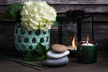 Spa 'da yeşil aroma çubukları koyu ahşap arka planda, hortensiya çiçekleri ve yanan mumlarla hayat bulur. Çakıl yığını