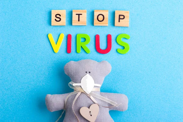 Teddy bear and drawn mask with Stop Virus sign in colorful letters on blue background