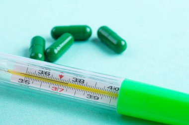 Yeşil kapsül haplarını şifalı bitkilerle ve yeşil nane arkaplanlı termometreyle aç. Sağlık ve dokunulmazlık koruması kavramı