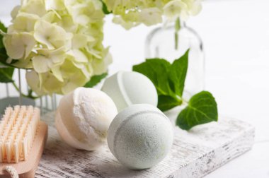 Spa 'da yeşil aroma bombaları beyaz ahşap arka planda hortensiya çiçekleri ve yapraklarla hayat buluyor.