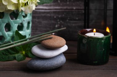 Spa 'da yeşil aroma çubukları koyu ahşap arka planda, hortensiya çiçekleri ve yanan mumlarla hayat bulur. Çakıl yığını