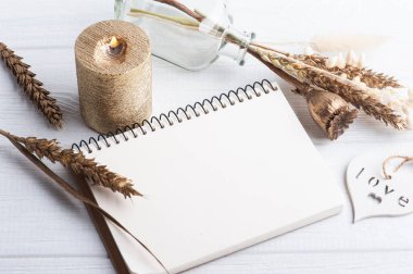 Boş bir defter, altın kuru çiçekler ve dekorasyon için yanan bir mum. Tatil ya da ahşap kalpli düğün organizatörü konsepti