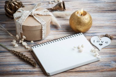 Boş bir defter, altın kuru çiçekler ve dekorasyon için yanan bir mum. Tatil ya da ahşap kalpli düğün organizatörü konsepti