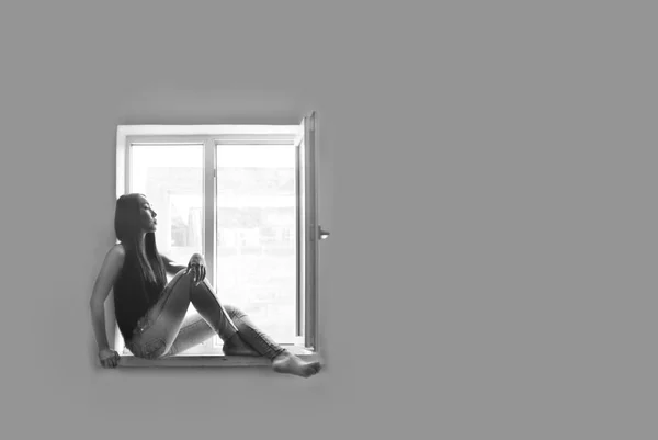 Modelo se sienta en un alféizar de la ventana contra una pared gris — Foto de Stock