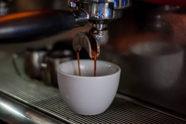 Kahve makinesinin başlığının altında bir fincan kahve. Kahve makinesiyle espresso yapıyorum. Kahve makineden akıyor. Taze kokulu espresso..