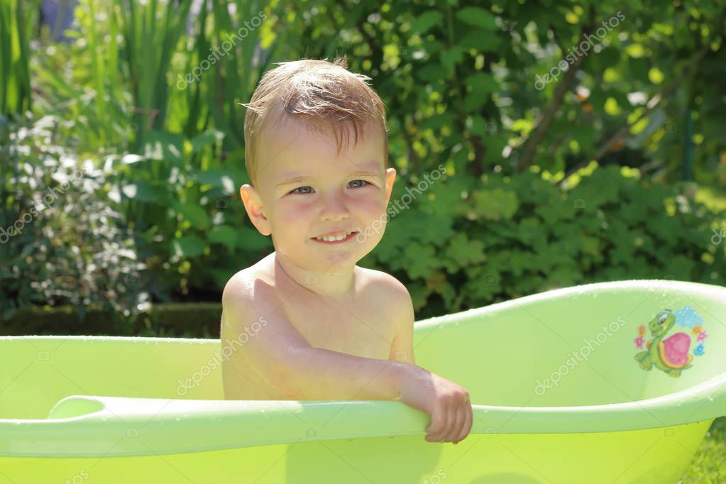 Baby bathes in a small green plastic tub in the garden. Summer