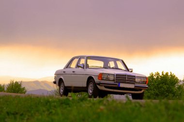 CLUJ-NAPOCA, 5 Ağustos 2011: Klasik Mercedes-Benz W 123 beyaz sedan araba gün batımında doğada