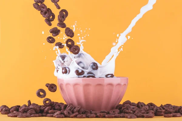 黄色の背景にミルクカップ チョコレートシリアルが周りに落ち ミルクが飛び散ると — ストック写真