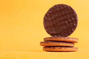 Çikolata kaplı kurabiye. Sarı arkaplanlı 4 kurabiye yığını..