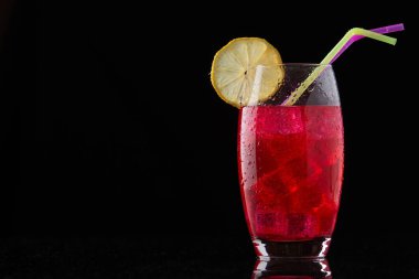 Buzlu kırmızı içki, siyah arka planda pipet ve limon.