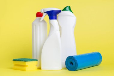 Üç kutu temizlik spreyi ve sarı bir arka plana yerleştirilmiş çöp torbası.