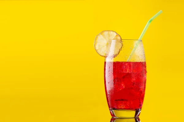 glass of soft drink with a lot of ice a slice of lemon and a straw on yellow background