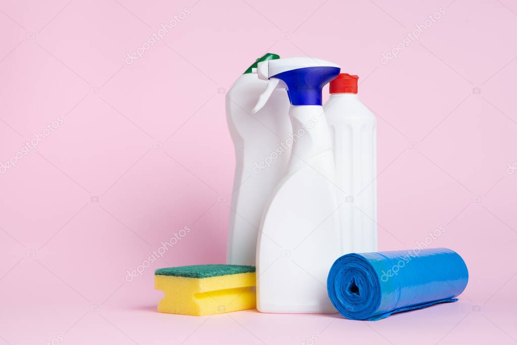 Three cans of cleaning  products spray with a scouring pad and garbage bags placed on a pink background