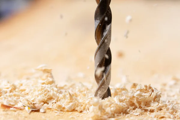 close-up view of a drill bit drilling a wood and chips jumping