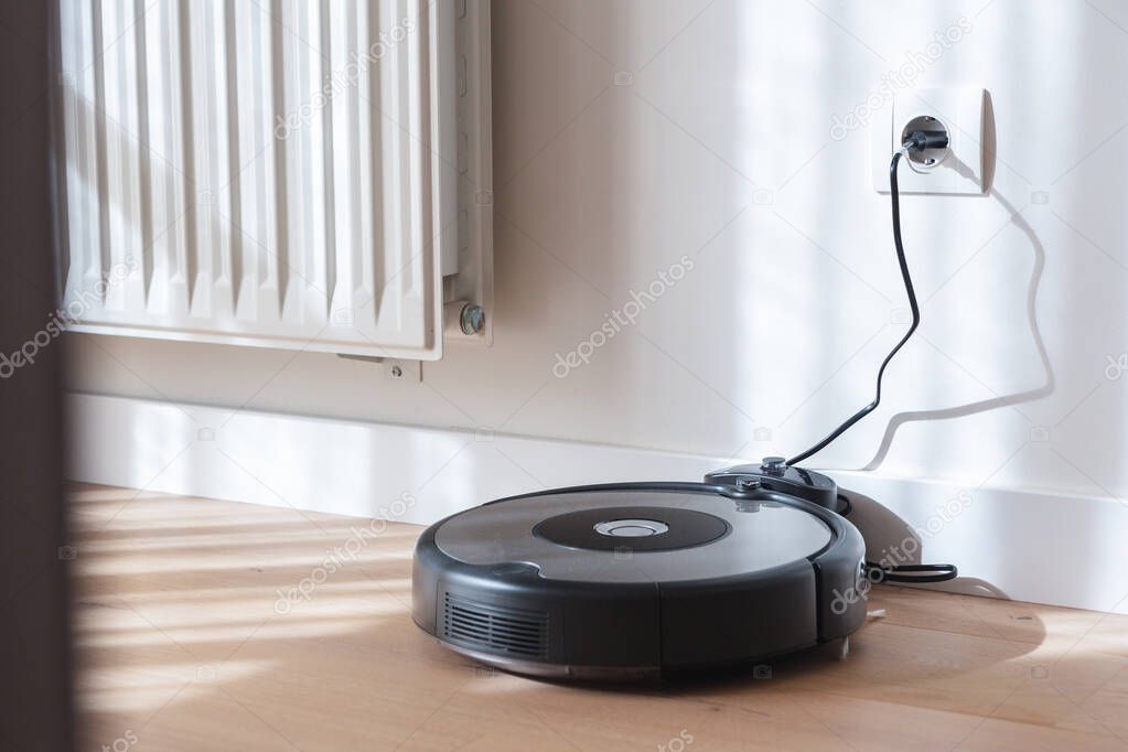robot vacuum cleaner charging in the charging base. Wood floor and white wall