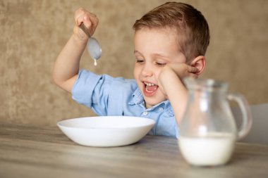 Sevimli Avrupalı bir bebek kendi başına yulaf lapası yiyor. Çocuk yulaf lapasını sevmiyor. Kaşıkla oynamak süt dökmektir. Çocuk eliyle başını tutuyor. Sağlıklı çocukları yeme kavramı. Odada..