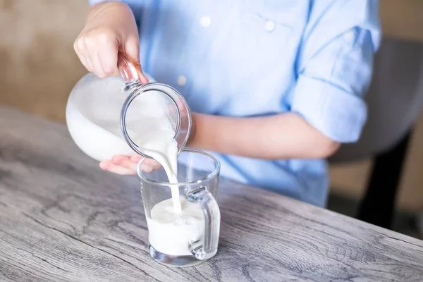 close-up hands of a child pour milk from a glass jug into a mug. Milk flows beautifully into a mug, with a thin stream