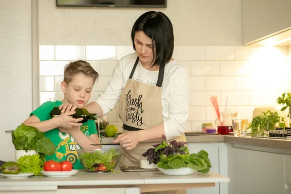 Anne ve oğlu mutfakta birlikte yemek pişiriyorlar. Yetişkin bir çocuk anneme sebze salatası hazırlamasında yardım ediyor. Çocuk yeşil sebzelere zeytinyağı döküyor. Sağlıklı yaşam tarzı kavramı