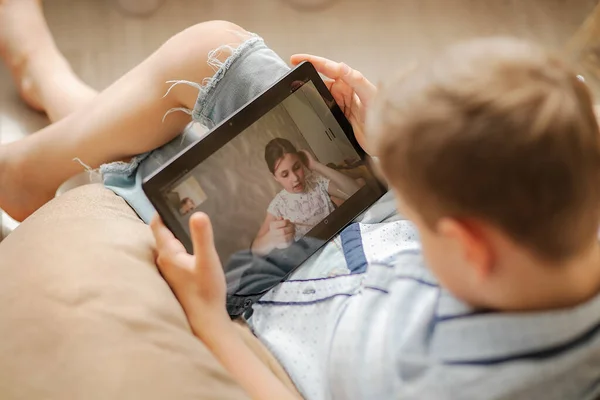 Tablet ekranı kapat. Tabletin ekranındaki kız sınıf arkadaşına çevrimiçi ev ödevlerini açıklıyor. Çocuklar evde karantinaya alındı. Bilgisayar İletişimi