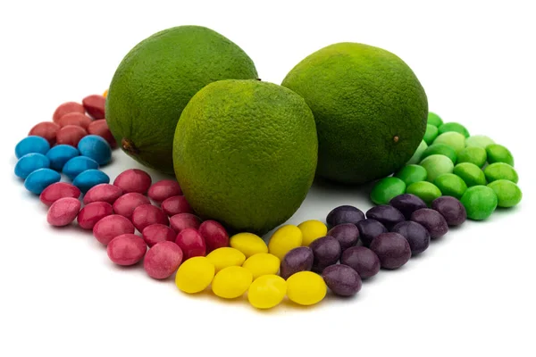 Renkli şekerler arasında beyaz bir arka planda üç taze limon.