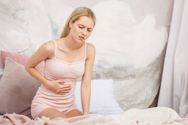 Genç kadın yatakta evde otururken karın ağrısı muzdarip. Mide ağrısı. Stres.