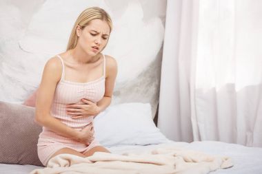 Genç kadın yatakta evde otururken karın ağrısı muzdarip. Mide ağrısı. Stres.