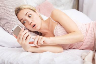 Dedikodu onun smartphone--dan gönüllülük yatakta hayran şok kadın portresi. Çok hızlı internet hızını