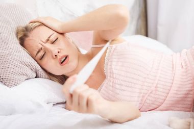Kadın yatakta yatan gribi virüsü ile o bir termometre ve alnına dokunmak onun Sıcaklığı ölçme