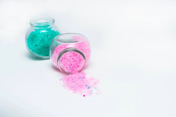 Açık pembe ve turkuaz banyo tuzlu iki şeffaf kavanoz. Beyaz arka planda yatay fotoğraf. Kişisel bakım ve spa için aksesuar konsepti. Açık pembe tuzlu banka yatar.