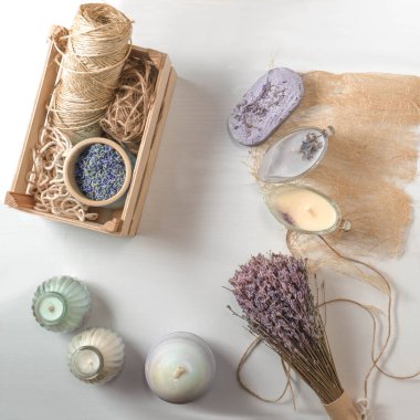 Düz kompozisyonda, ahşap bir zeminde, kurutulmuş lavanta çiçekleri, mor ve krem mumlar bulunan el yapımı sabun kalıbı vardı. Ahşap bir kutuda lavanta çiçekleri ve ahşap aksesuarlar.