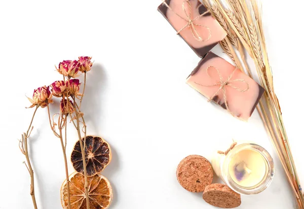 Düz kompozisyon, iki el yapımı kahverengi pembe sabun ile portakal rengi, kurumuş portakal dilimleri, gül çiçekleri, pastel vanila mumu ve ahşap desenli buğday başaklarıyla birlikte. Yatay fotoğraf. 